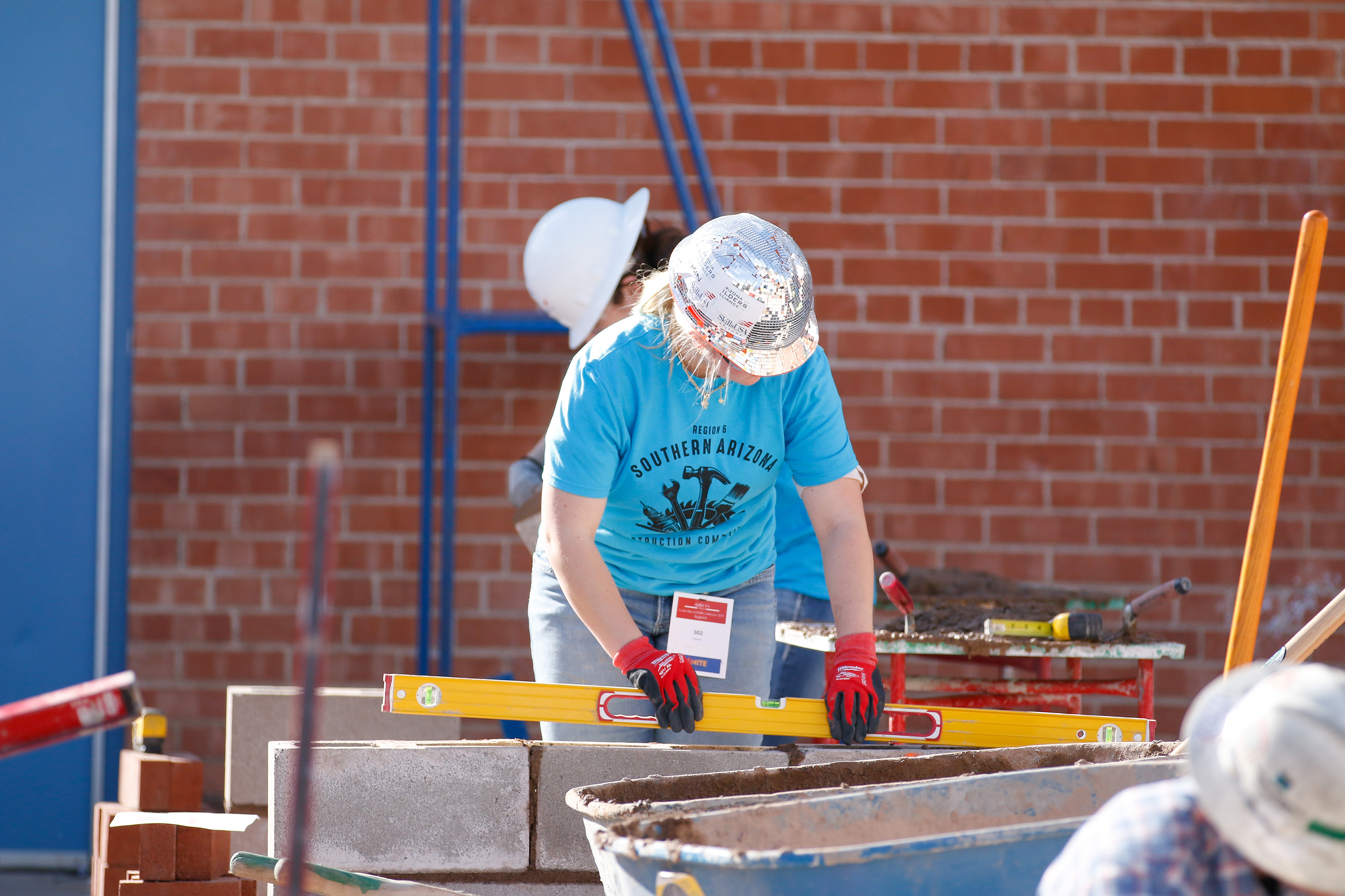 A girl in a sparkly hard hat measures some wood