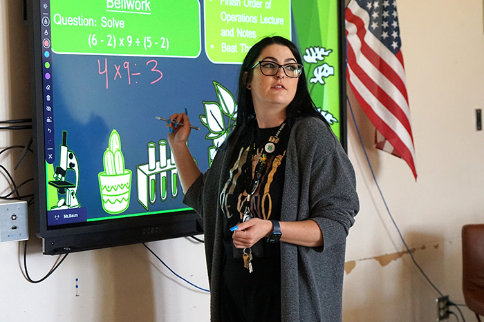 A teacher turns around to her class as she writes on a smart board