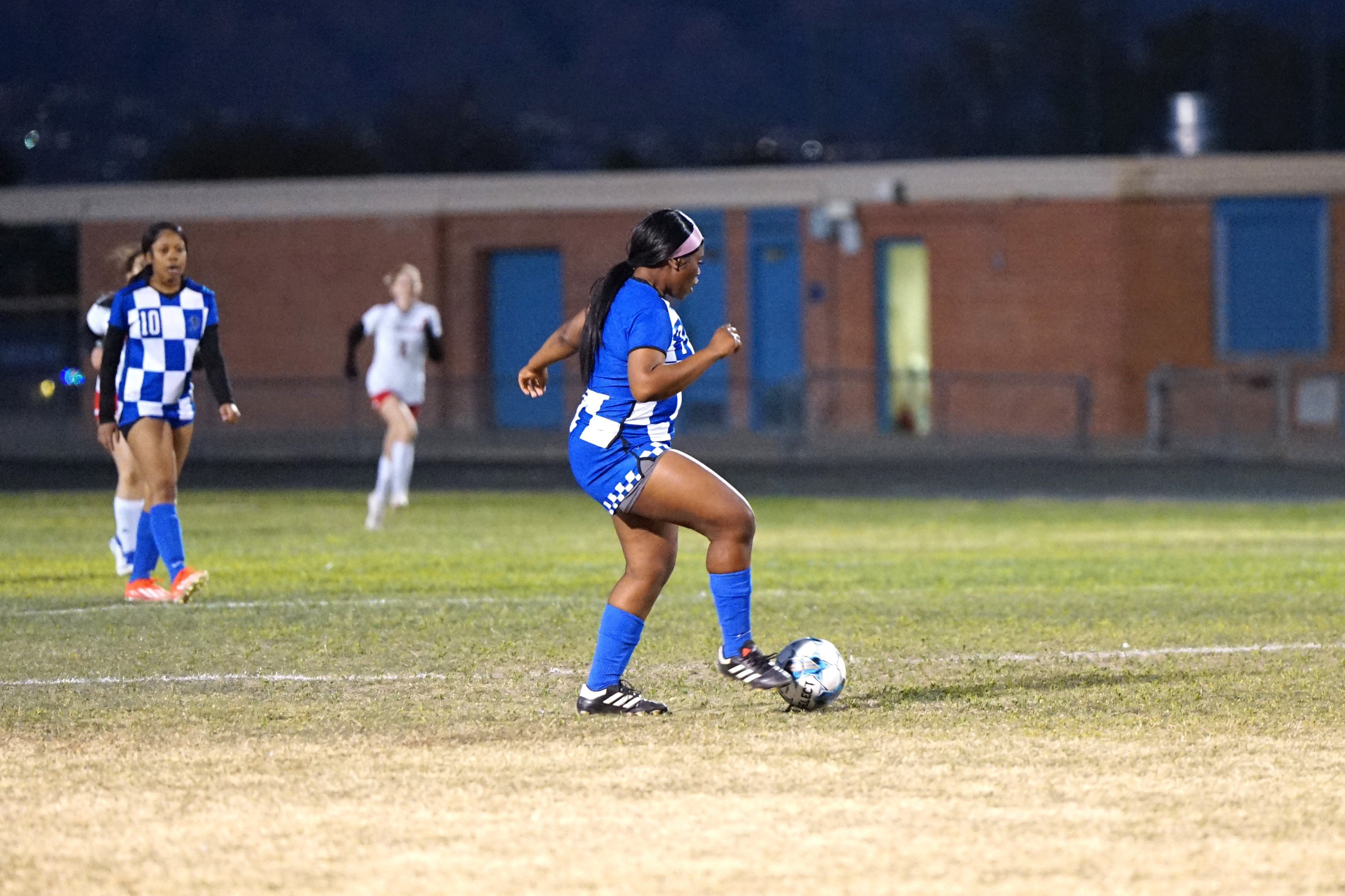 A girl in a blue uniform gets ready to kick the soccer ball to a teammate