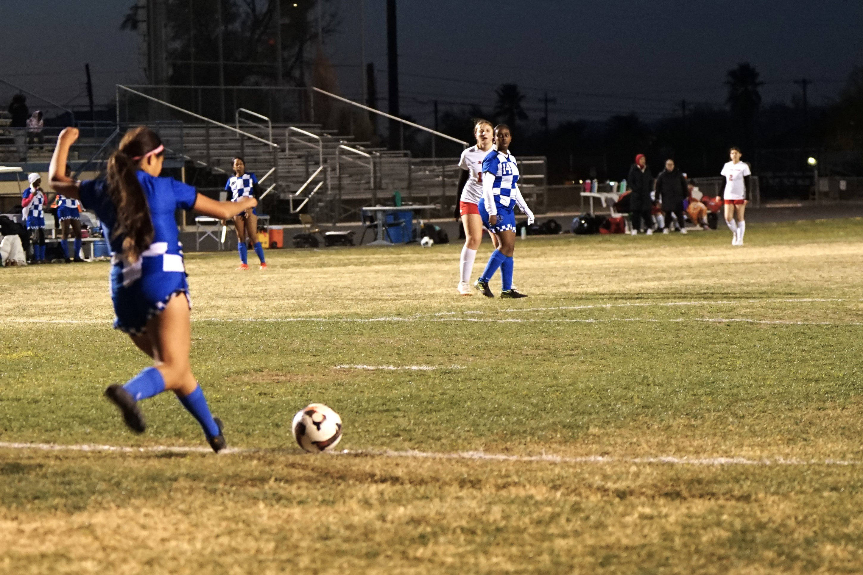 A girl in a blue uniform kicks a soccer ball across the field