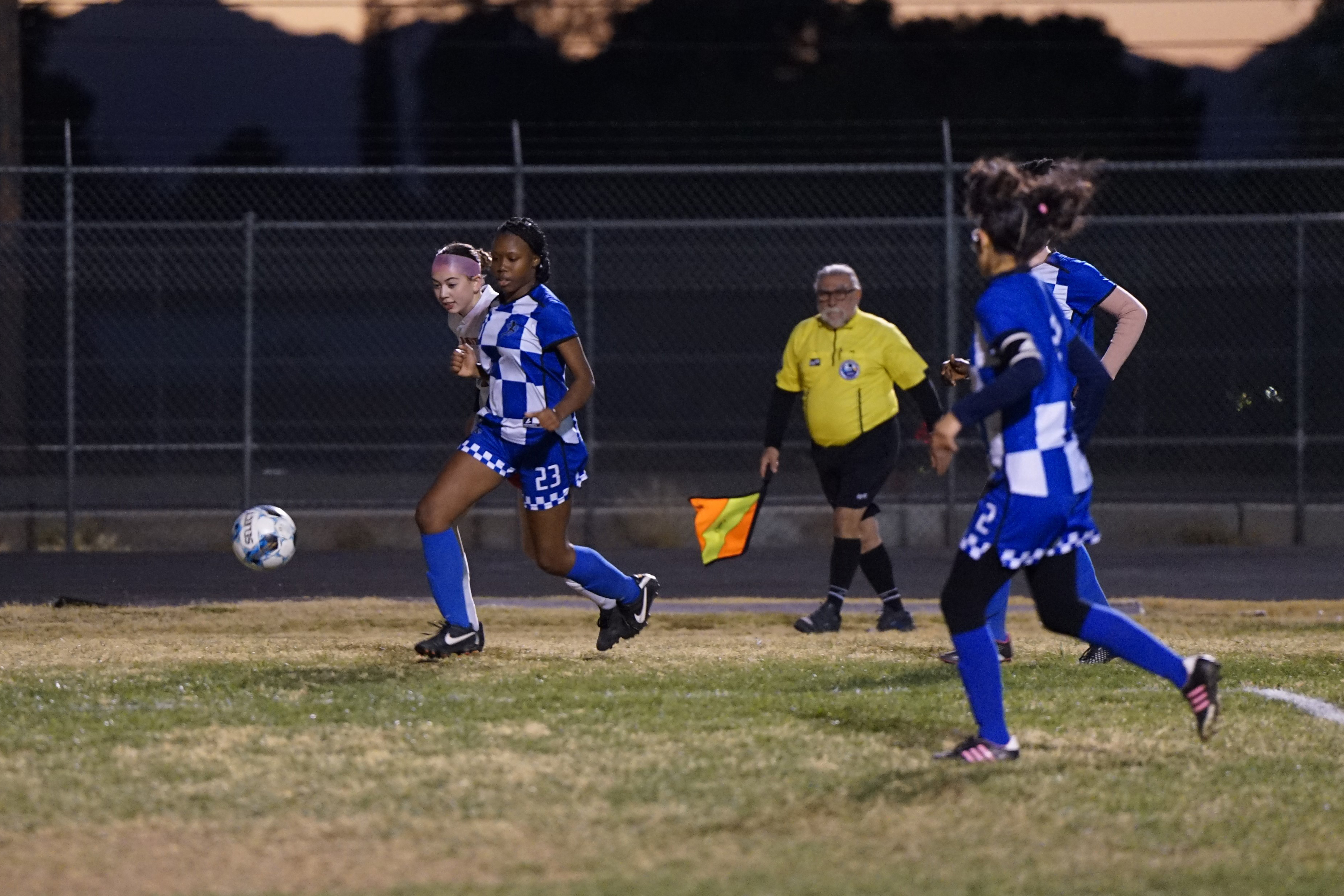 Girls in blue uniforms chase the soccer ball