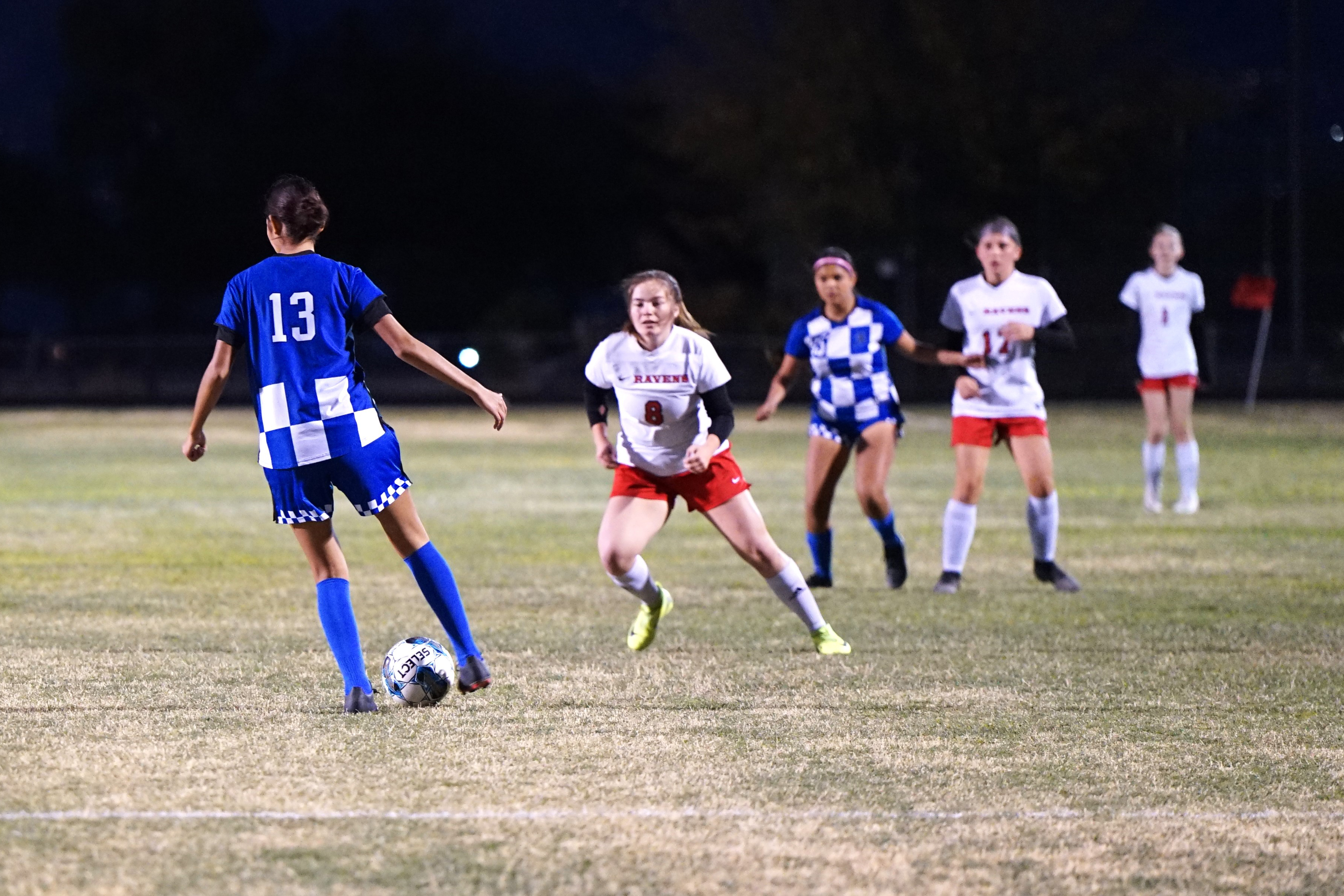 A girl in a blue uniform tries to keep the soccer ball away from the other team