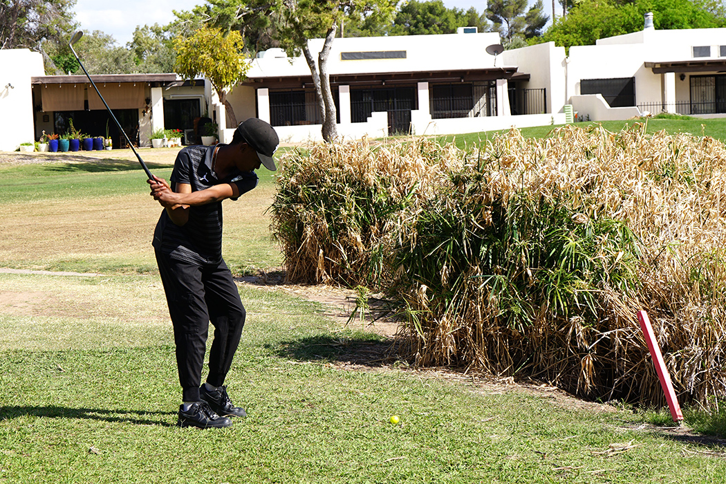 A boy swings his golf club towards some houses