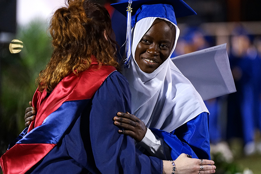 A teen girl in a head covering and graduation cap and gown hugs a woman