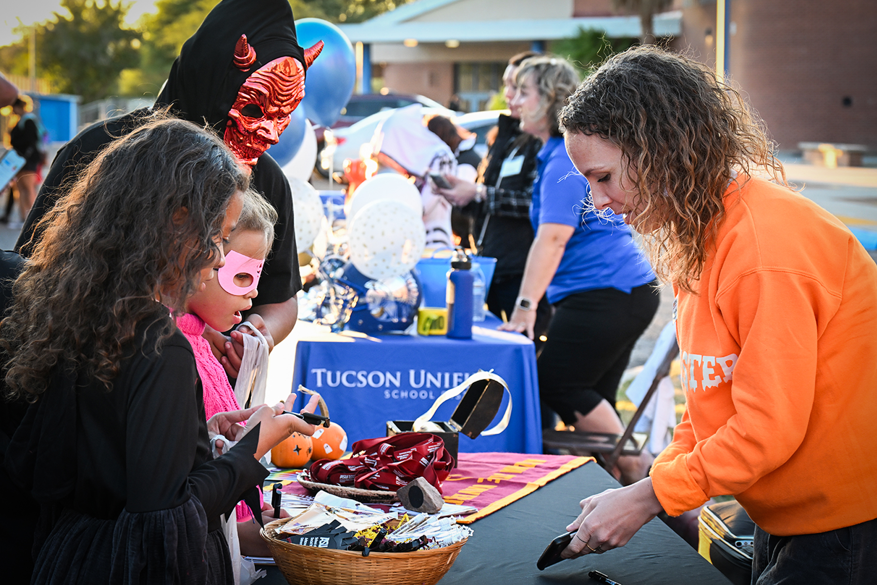 Three kids in costumes pick out treats at one of the tables