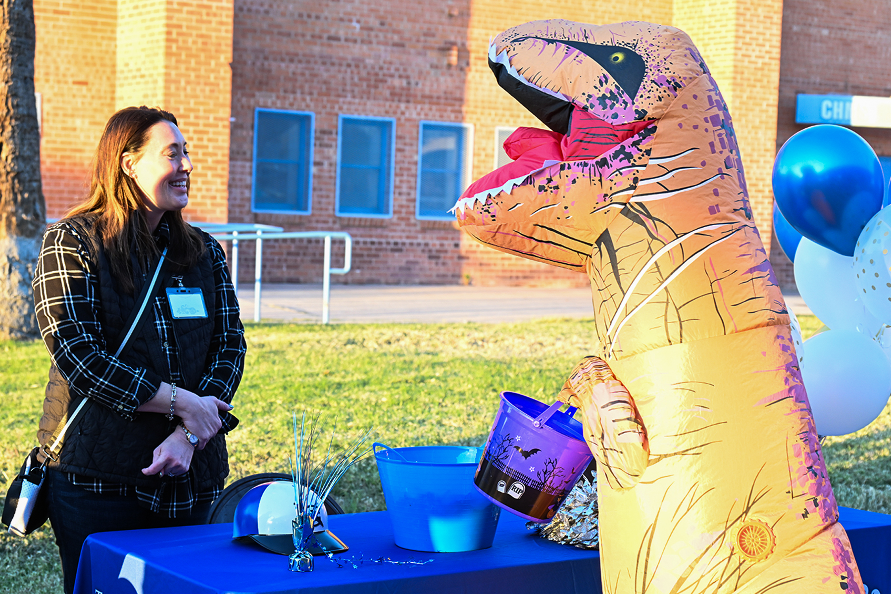 A child in an inflatable dinosaur costume visits a table