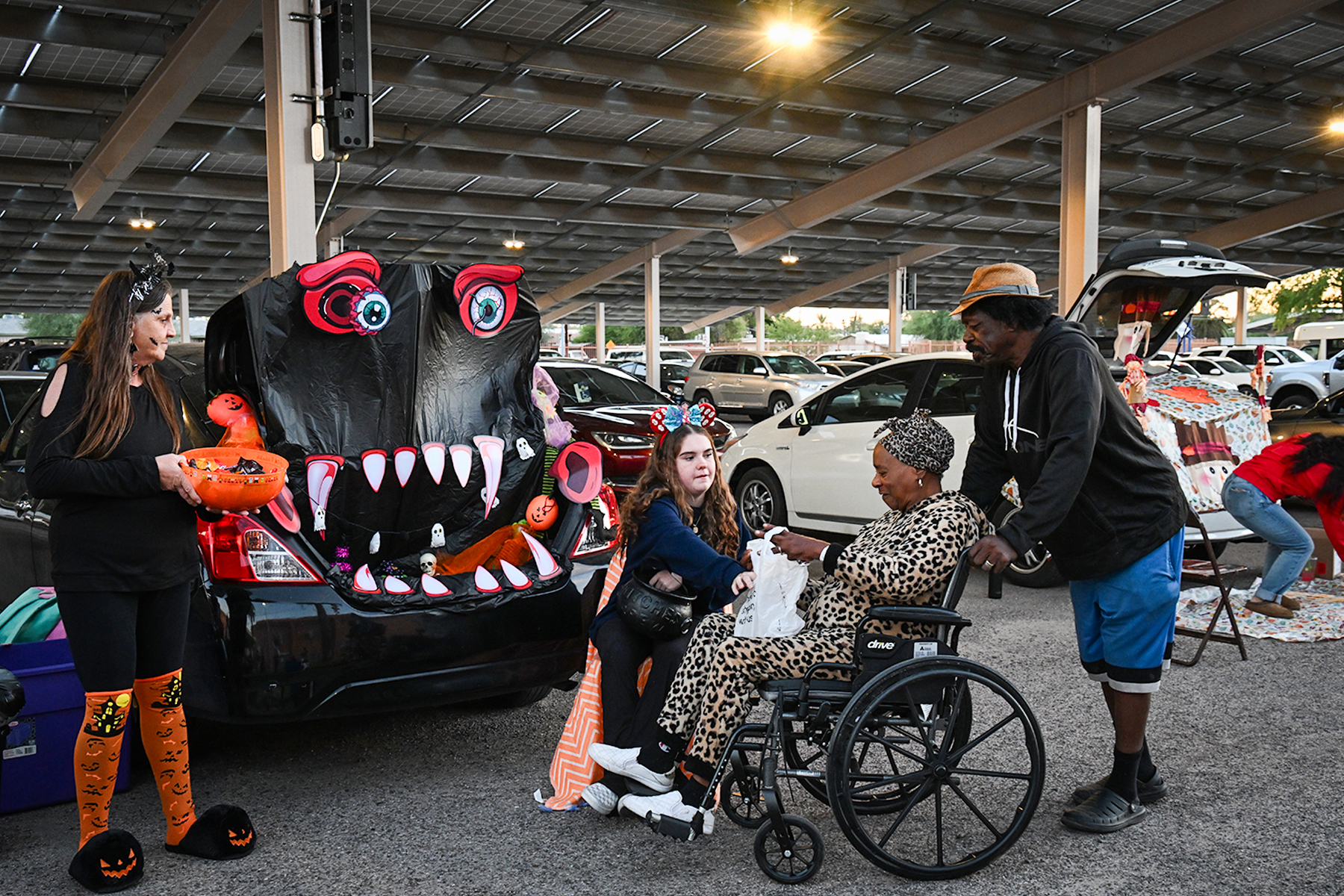 A woman in a wheelchair gets candy from students handing out treats from their car decorated like a monster