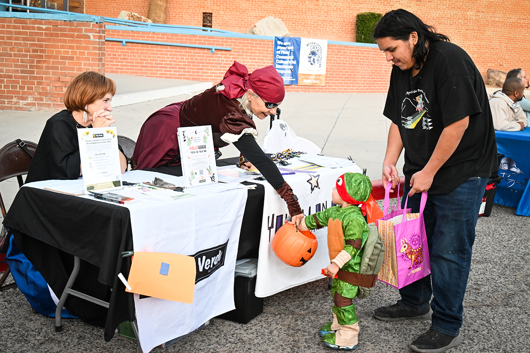 A little boy in a Ninja Turtles costume gets candy from a woman dressed as a pirate