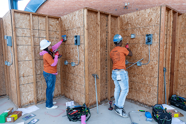 Students in hard hats drill into boards to install electrical boxes