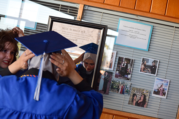 A graduate adjusts her cap in the mirror