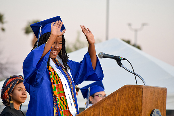 A graduate puts up her hands in excitement at the podium