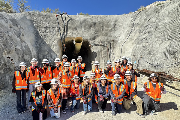 Students wearing hard hats and orange safety vests pose for a group photo outside the mine