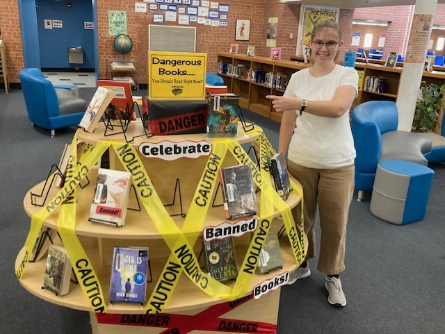 A teen girl smiles and points to the display she made of banned books