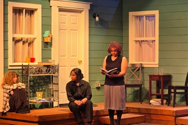 Two students perform on stage in front of a house backdrop