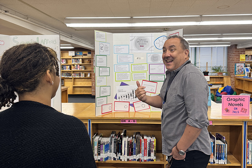 A teacher talks excitedly with his students as he shows off one of their science fair posters