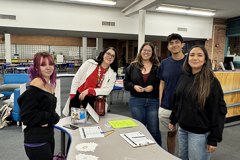 Four students and their teacher smile for a photo around a table in the library