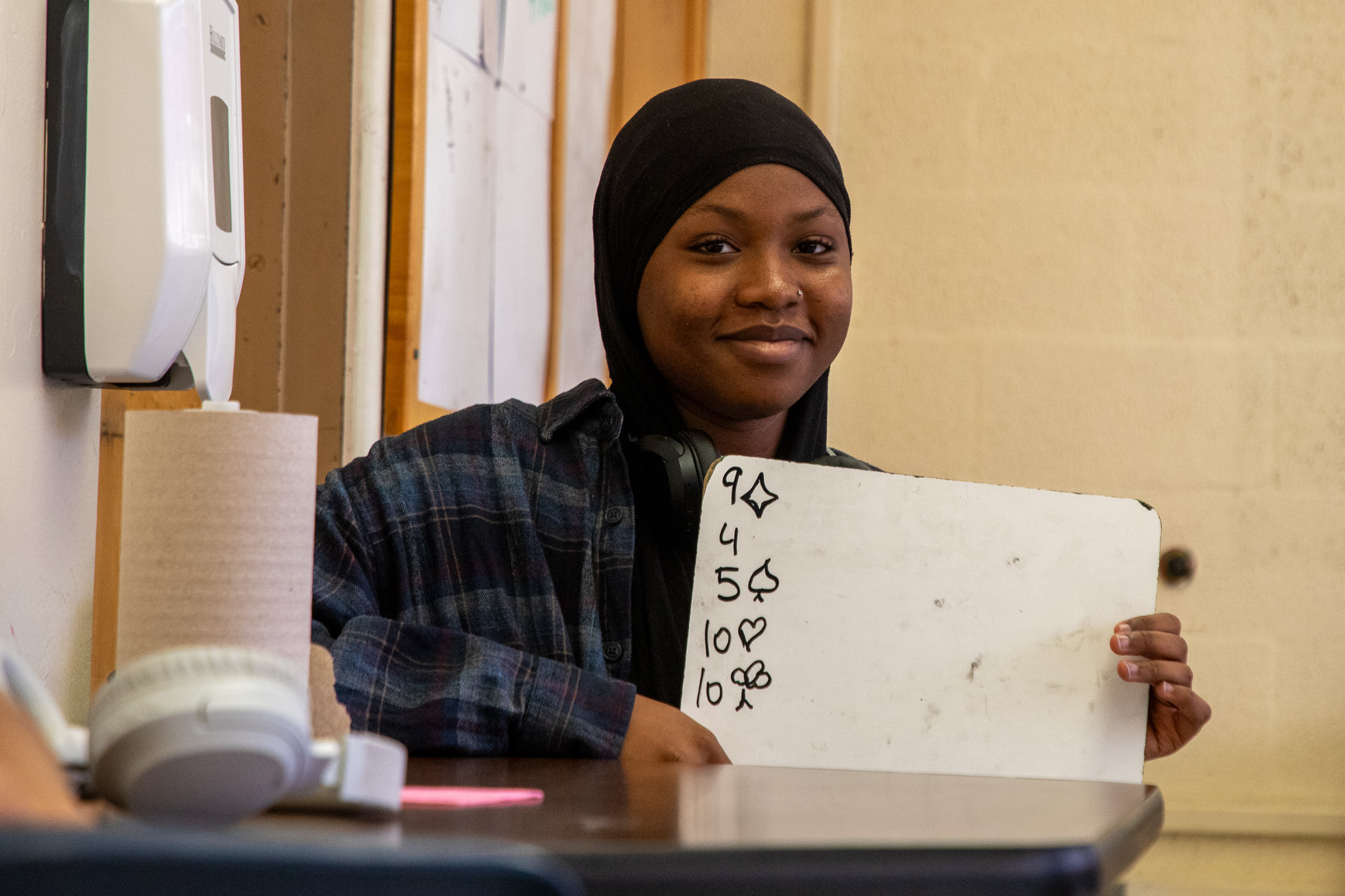 A teen girl in a black headscarf holds up her whiteboard