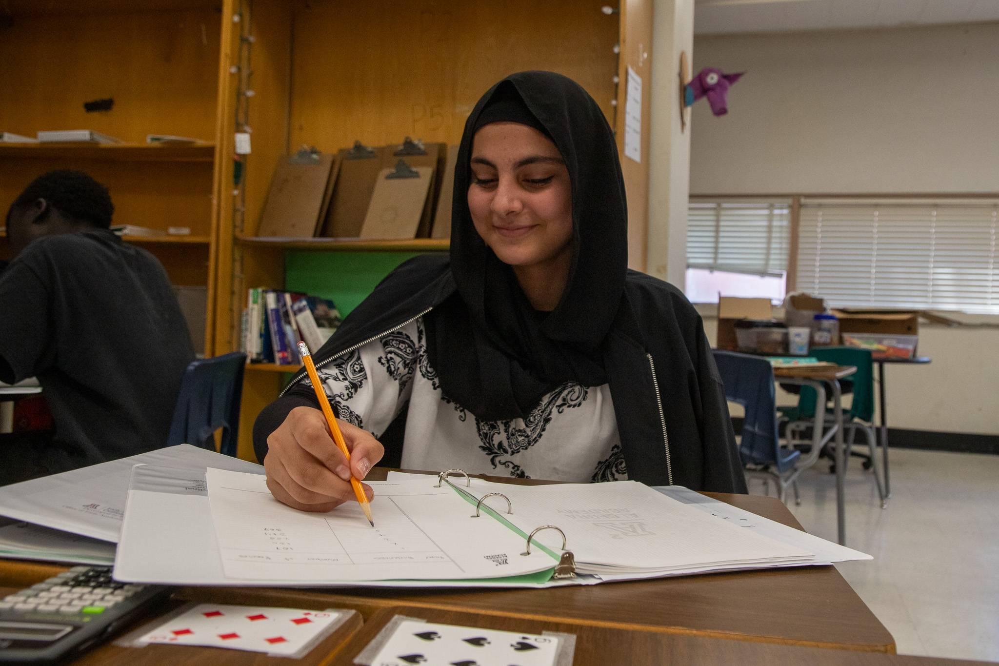 A teen girl in a black headscarf writes in her notebook