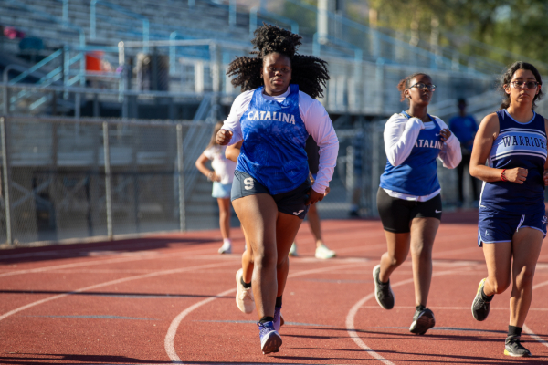 Two teen girls in blue Catalina singlets and white long sleeves run around the track