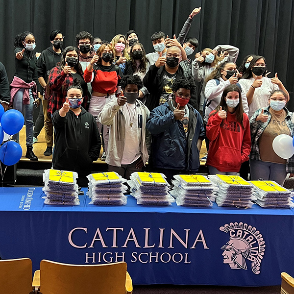 Large group of stidents with thumbs up standing behind a table full of laptops that has a Catalina High School Tablecloth on it